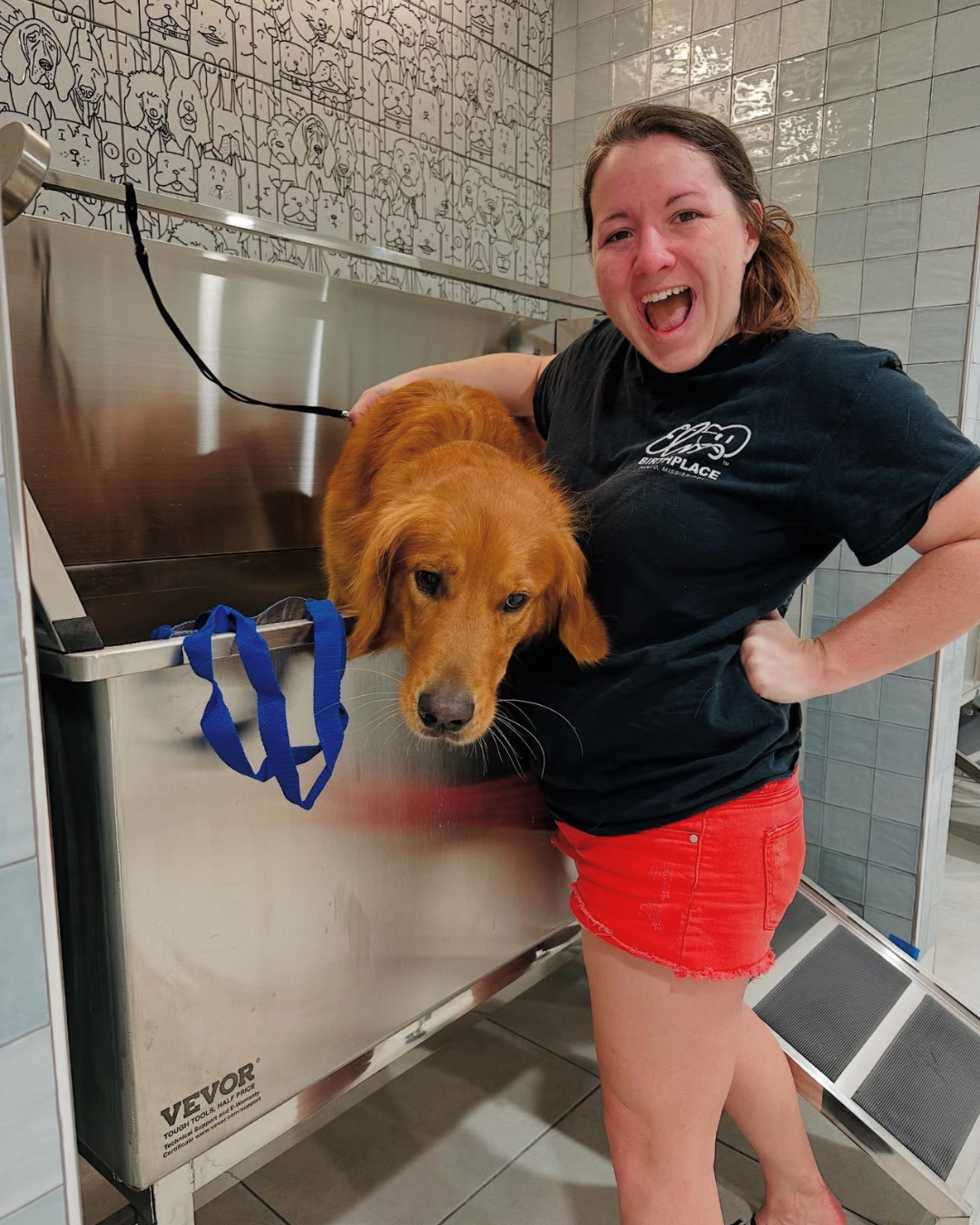 A resident smiling with a golden retriever in the dog wash station at The Pulse OKC.