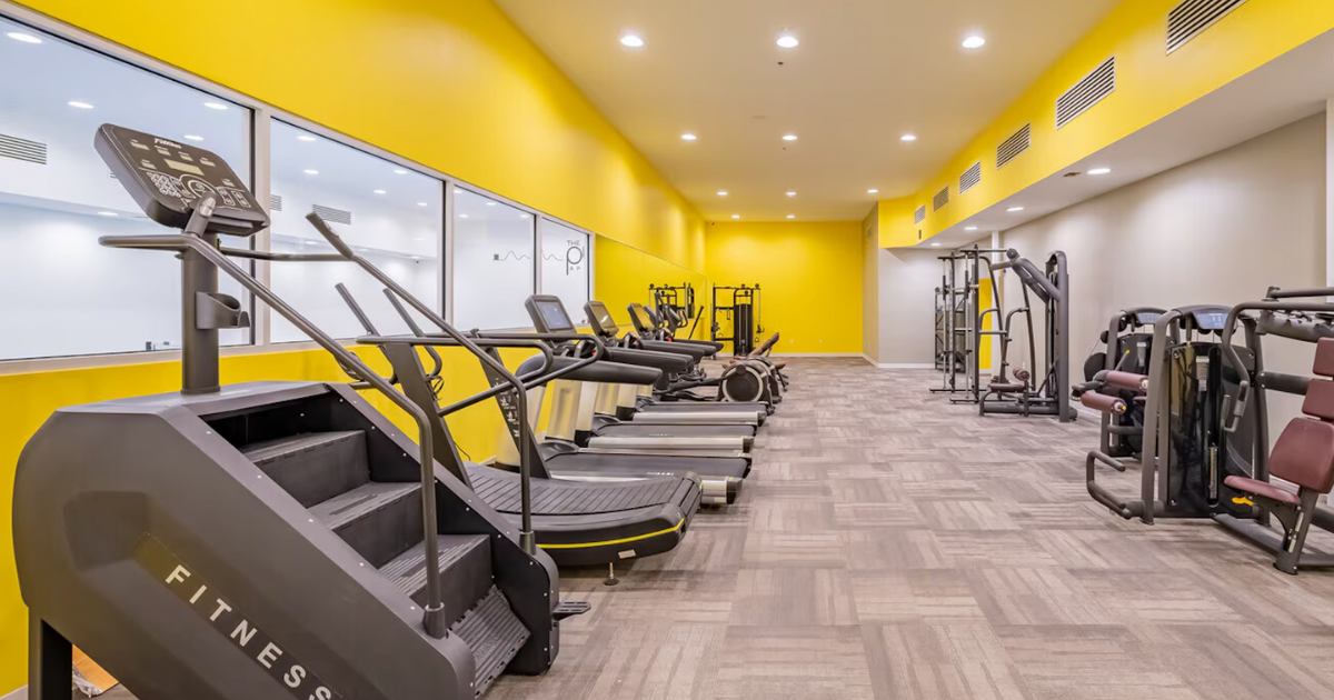 The yellow fitness center at The Pulse OKC with cardio and strength equipment.